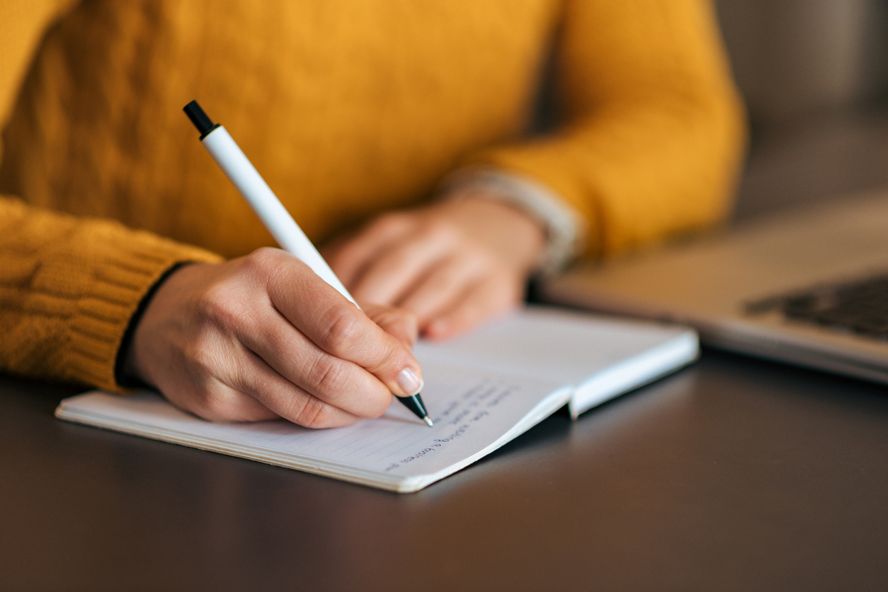 Vrouw in gele trui schrijft in een notitieboekje