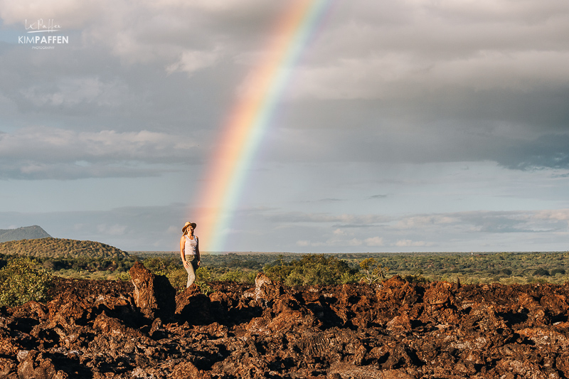Tessa standing in front of a rainbow on the Shetani Lava Flow in Tsavo West National Park Kenya