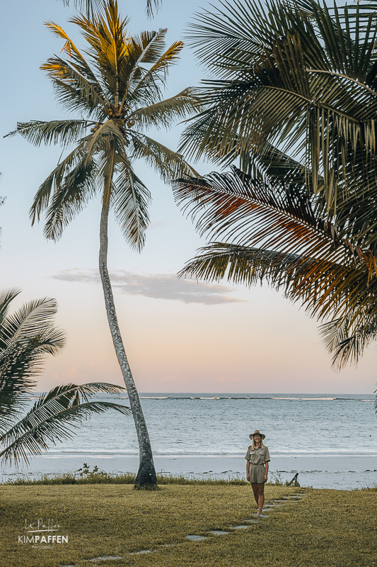 Tessa in the well-maintained garden of the Fisherman luxury beachfront villa on Diani Beach with a magical sunset and ocean in the back