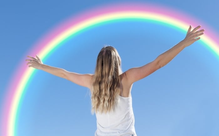 Vrouw in wit hemd voor een blauwe lucht met een regenboog