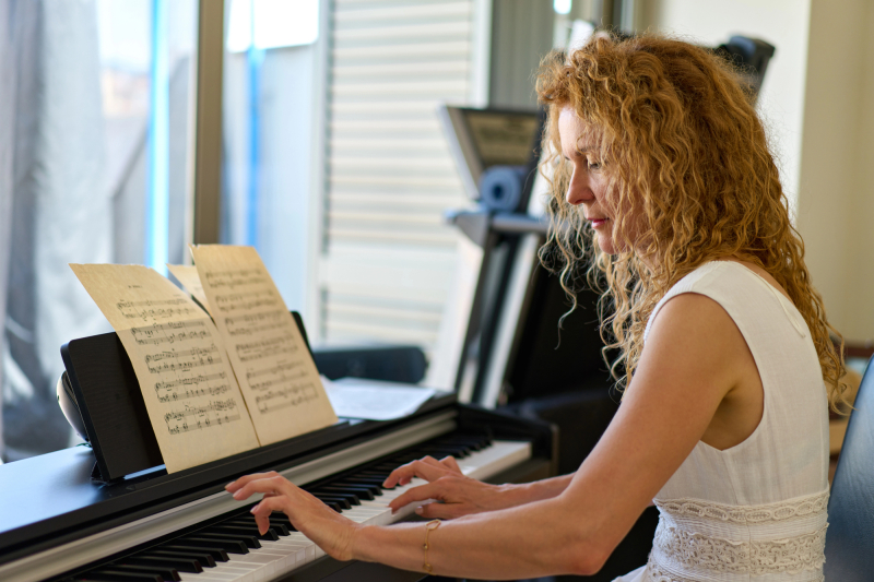Volwassen vrouw leert piano spelen zonder noten lezen, thuis achter de piano
