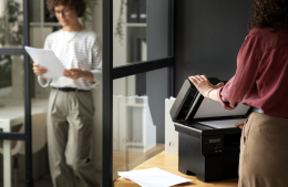 Kantoormedewerker print documenten terwijl collega wacht bij moderne printer.