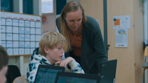 Leerkracht begeleidt een leerling één-op-één aan zijn tafel in een rustige klasomgeving