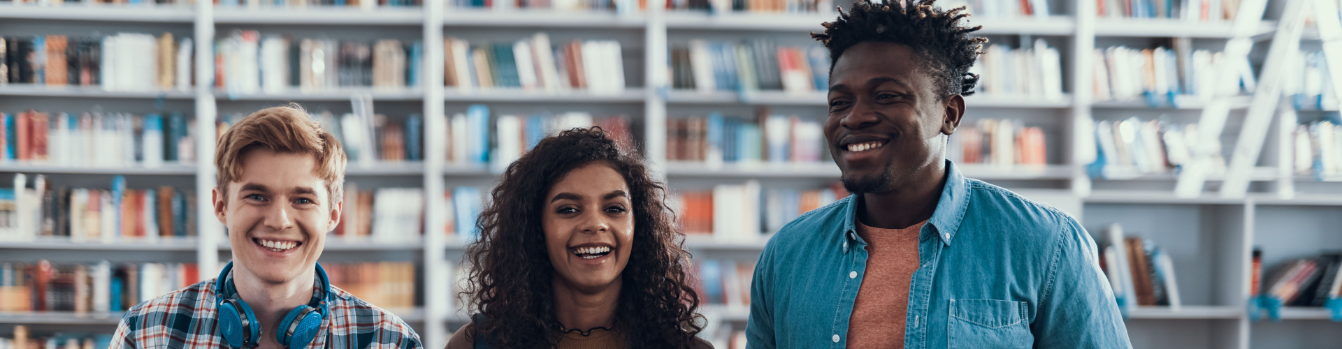 Drie volwassenen volgen een praktische NT2-les in een bibliotheek, met focus op gesprekken en dagelijkse situaties.