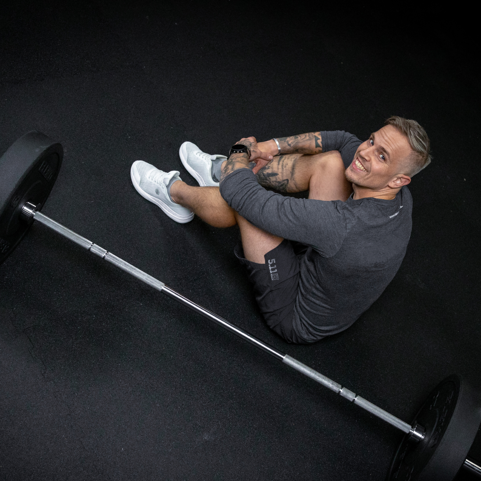 Een glimlachende personal trainer die op de grond zit met een barbell