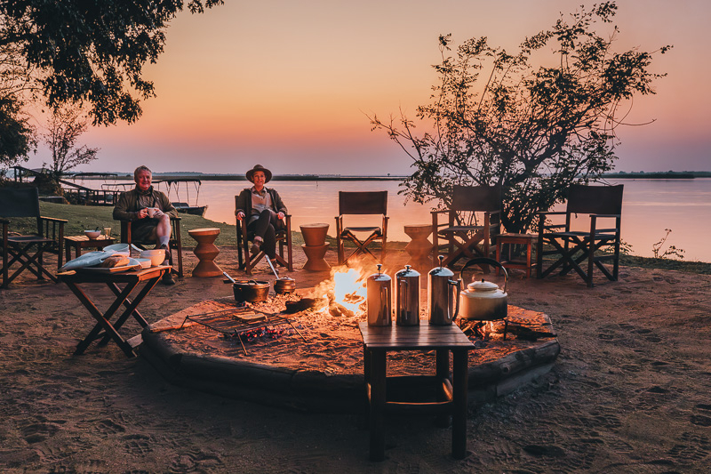 Kim and Denis at Chiawa Safaris sitting at the fire during sunrise before heading on a walking safari in Lower Zambezi