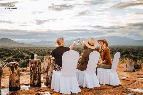 Safari-voertuig en gasten met sundowner drankjes bij Poacher’s Lookout, met wijds uitzicht over Tsavo’s savanne bij zonsondergang