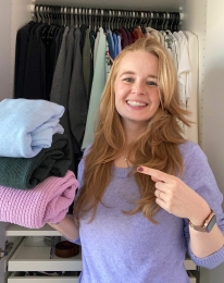 Opruimcoach / professional organizer Saskia van Amerongen staat lachend voor een open kledingkast.