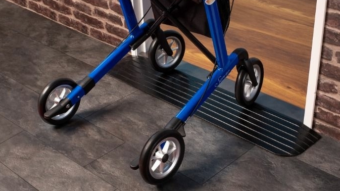 Een rollator die soepel over een zwarte drempelhulp rijdt bij een deurpost