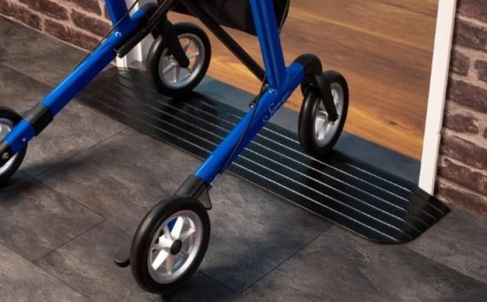 Een rollator die soepel over een zwarte drempelhulp rijdt bij een deurpost