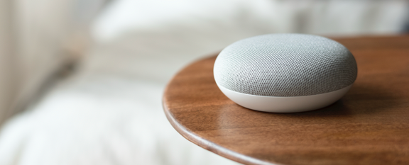 Slimme speaker Google Home op een houten tafel, gebruikt voor gemak en veiligheid bij zelfstandig wonen ouderen