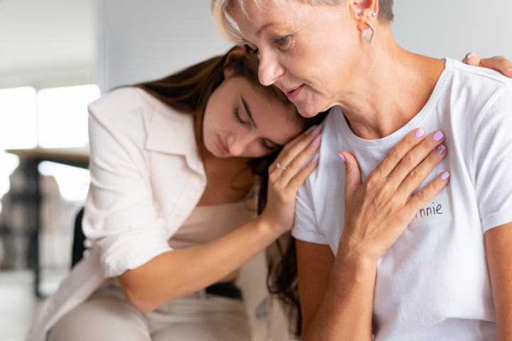 Vrouwelijke mantelzorger troost oudere vrouw met hand op schouder, emotioneel moment in huiselijke setting