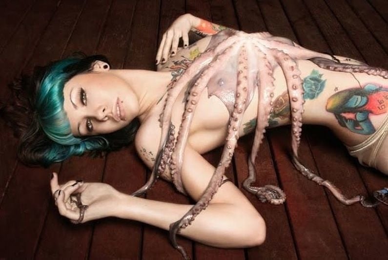 A woman lying on the floor covered with an octopus and tattoos