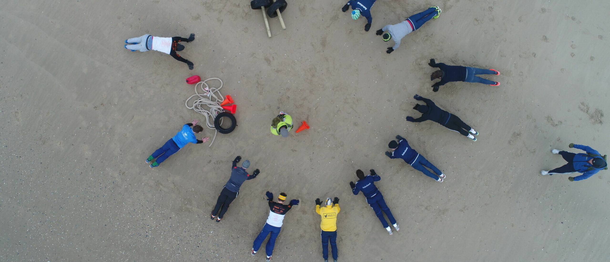 Groep deelnemers tijdens Bootcamp Beach op het strand van Texel in cirkelopstelling met sportmaterialen