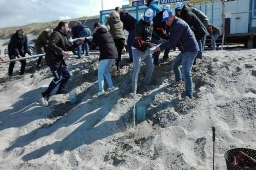 Groep mensen doet teamwork opdracht op het strand van Texel tijdens een groepsuitje