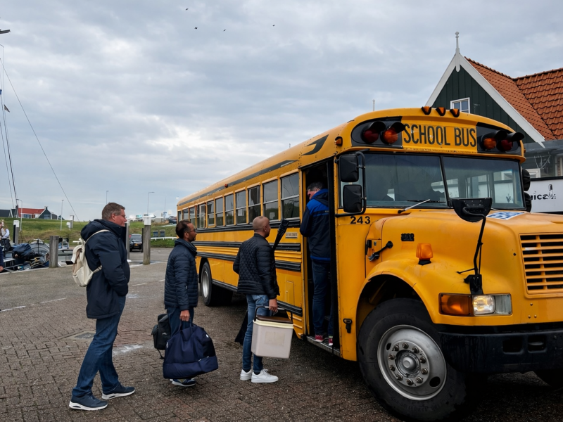 Groep stapt in Amerikaanse schoolbus voor groepsvervoer op Texel groep die instapt in een Amerikaanse schoolbus voor een teamuitje op Texel