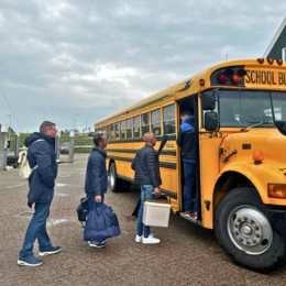 Groep stapt in Amerikaanse schoolbus bij de haven van Oudeschild voor groepsvervoer op Texel