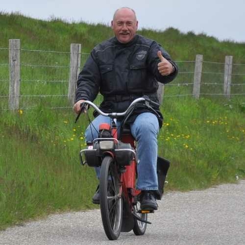 Lachende man rijdt op een klassieke rode solex over een landweg op Texel
