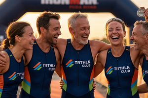 Een groep van vijf lachende triatleten in TRTHLN Club kleding deelt een overwinningsmoment bij de finish, waarbij de middelste atleet zijn medaille toont