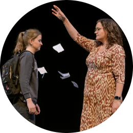 Moeder en kind in een indringend musicaltheatermoment, terwijl een verscheurde brief tussen hen in door de lucht dwarrelt.