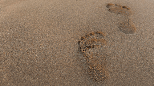 Hooghoekfoto van voetafdrukken op een zandstrand, illustratie van de reis naar persoonlijke ontwikkeling na verslaving.