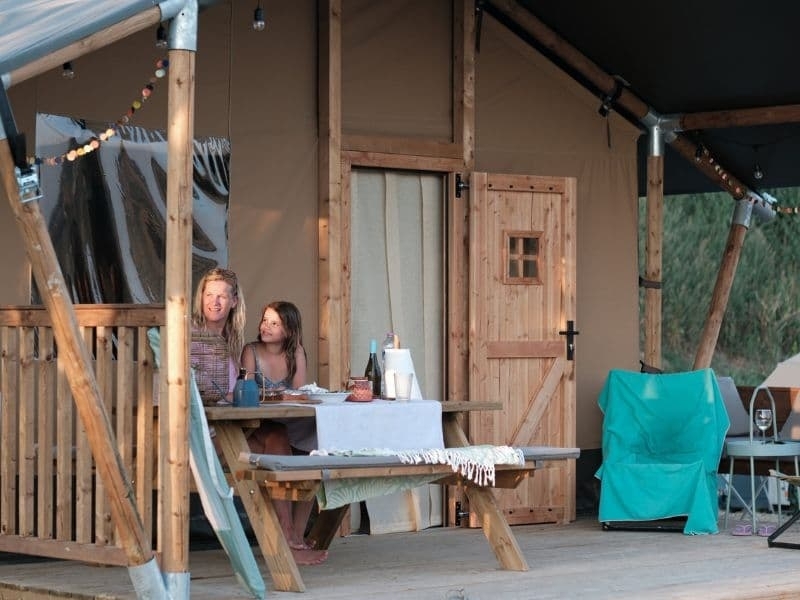 Moeder met kind zitten samen op de veranda van een safaritent tijdens een rustige avond bij Vista Fermo