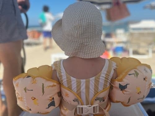 Jonge peuter met zwambandjes en hoedje kijkt uit over het strand in Le Marche tijdens een gezinsvakantie