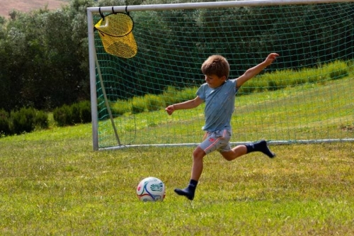 Voetballen op het veld van de camping Kind schiet op doel op het voetbalveld van Vista Fermo, met olijfbomen en de heuvels van Le Marche op de achtergrond.