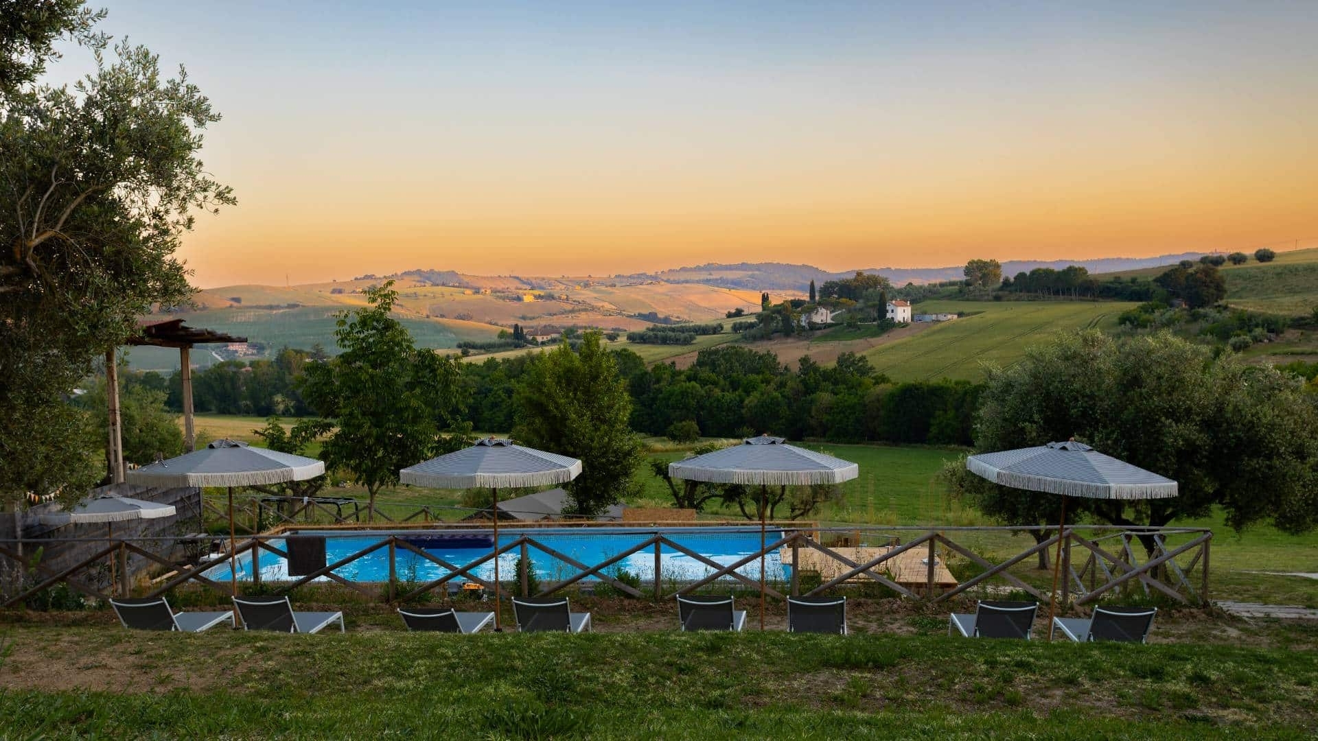 Zwembad met panorama over de heuvels bij zonsondergang Zwembad met ligbedden en parasols op Vista Fermo, met een weids panorama over de olijfbomen en glooiende heuvels van Le Marche bij zonsondergang.