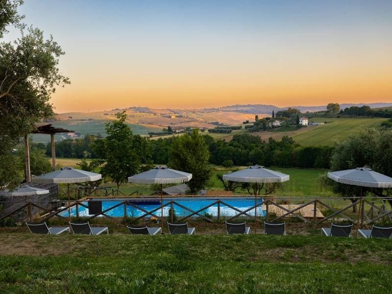 Zwembad met ligbedden en parasols op Vista Fermo bij zonsondergang, met een gouden uitzicht over de glooiende heuvels van Le Marche.