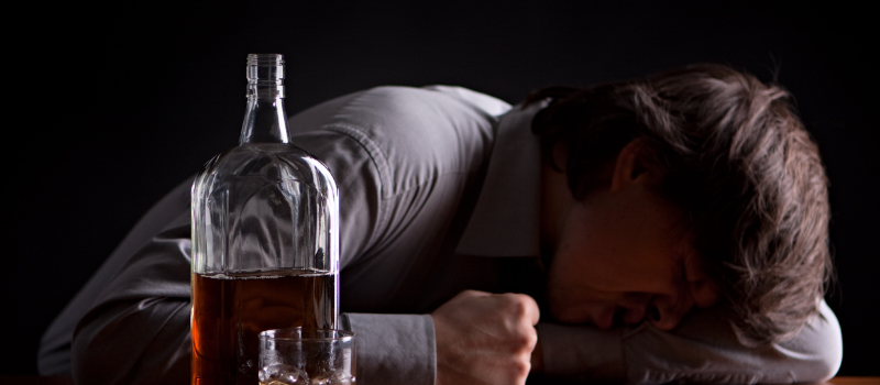 Man ligt voorover met fles alcohol en glas op tafel