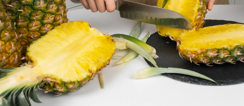 Hand snijdt verse ananas in helften op snijplank, tropisch fruit bereiden