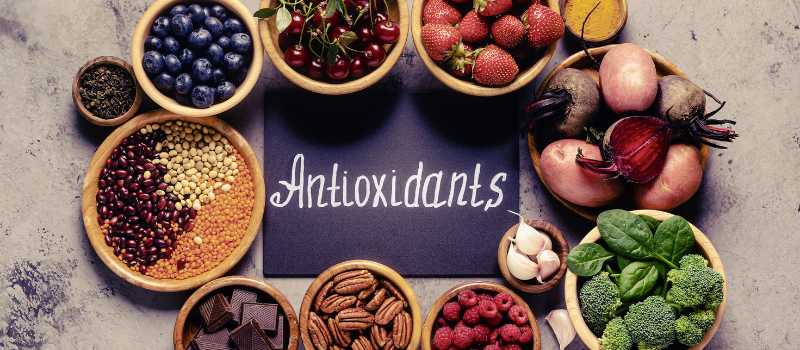 Diverse antioxidant-rijke voedingsmiddelen in schalen rond een bord met het woord 