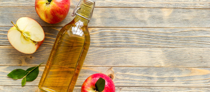 Fles appelciderazijn en verse appels op houten ondergrond, gezonde keukeningrediënten