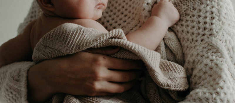 Baby ligt op schoot onder deken, kwetsbaar voor kinkhoest