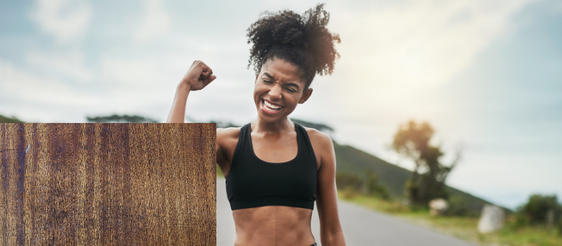 Een lachende vrouw in sportkleding heft haar arm triomfantelijk op tijdens een buitentraining.