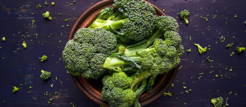 Verse broccoli in een bruine schaal op een donkere ondergrond.