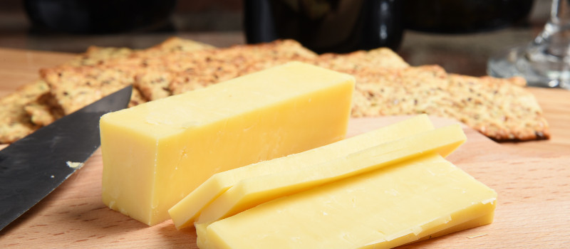 Gesneden cheddar kaas op houten plank met crackers