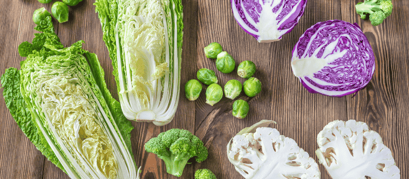 Diverse groenten op een houten ondergrond, waaronder Chinese kool, rode kool, spruitjes, broccoli en bloemkool.