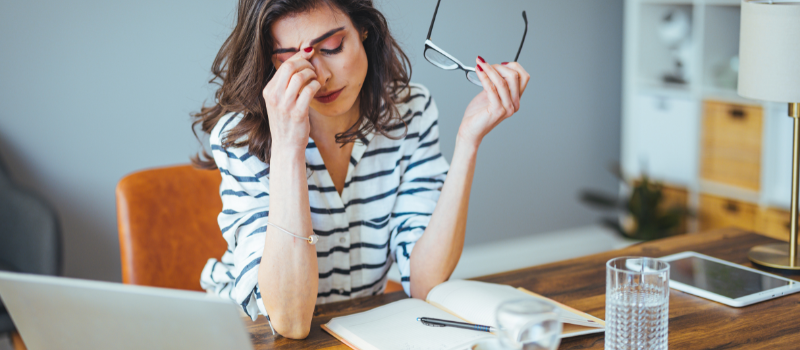 Vermoeide vrouw met hand op hoofd tijdens werk, chronische vermoeidheid