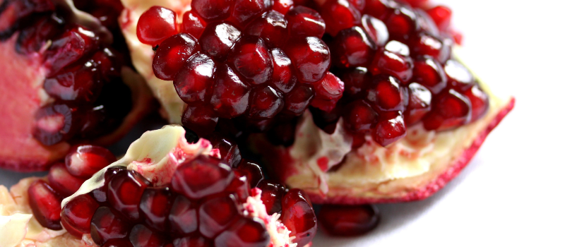 Close-up van sappige granaatappelpitten in schil op witte achtergrond, gezond fruit