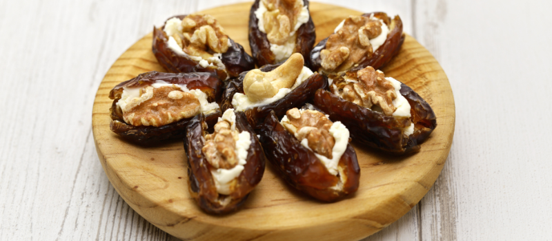 Gevulde dadels met walnoten, cashewnoten en geitenkaas op een houten bord.