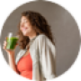 Lachende vrouw drinkt groene smoothie in keuken met vers fruit