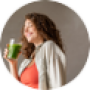 Lachende vrouw drinkt groene smoothie in keuken met vers fruit