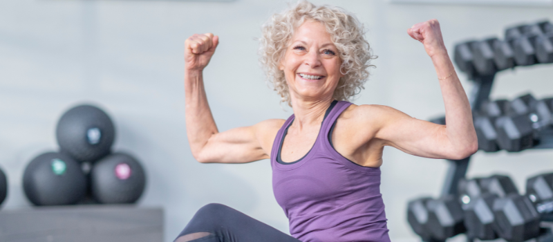 Lachende seniorenvrouw in sportschool die kracht toont, gezondheid en fitheid.