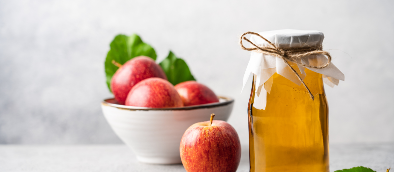 Glasfles met appelciderazijn naast kom rode appels op witte achtergrond, natuurlijk product