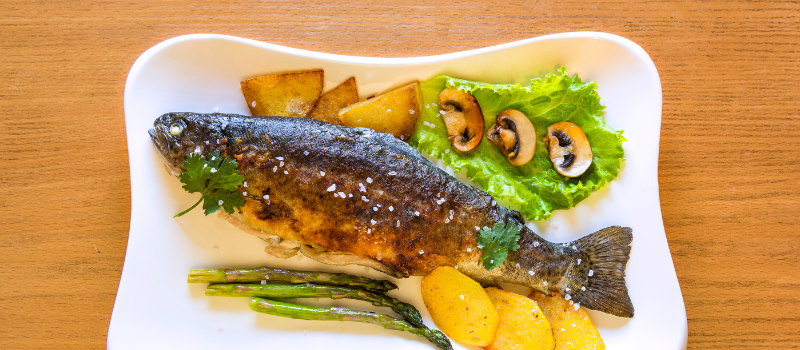 Gebakken forel geserveerd met asperges, aardappel en champignons