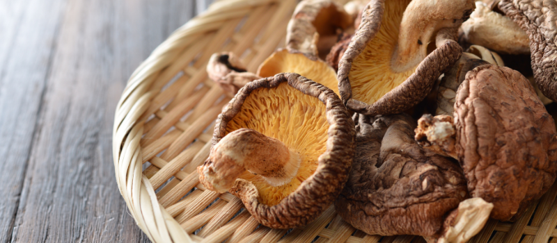 Gedroogde shiitake paddenstoelen in een rieten mandje op een houten tafel.