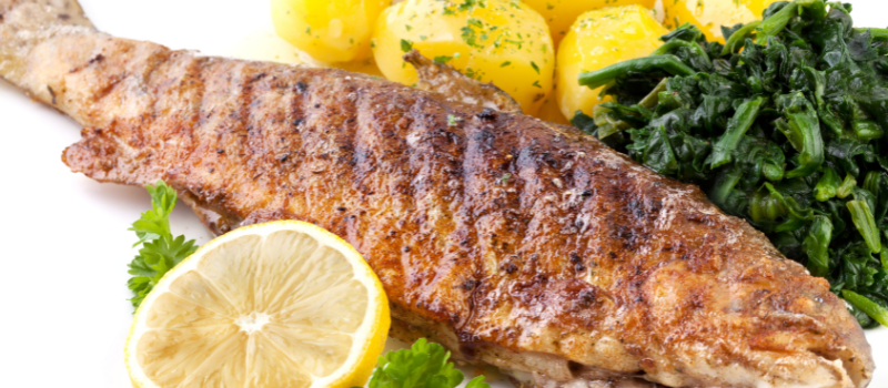 Gegrilde forel met citroen, spinazie en aardappelen op bord