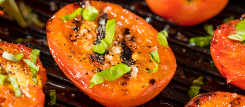 Gegrilde tomaten met verse basilicum op een barbecuegrill.